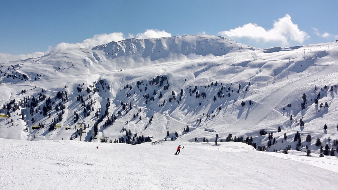 Snow-covered mountain landscape with skiers under a blue sky and sunshine.