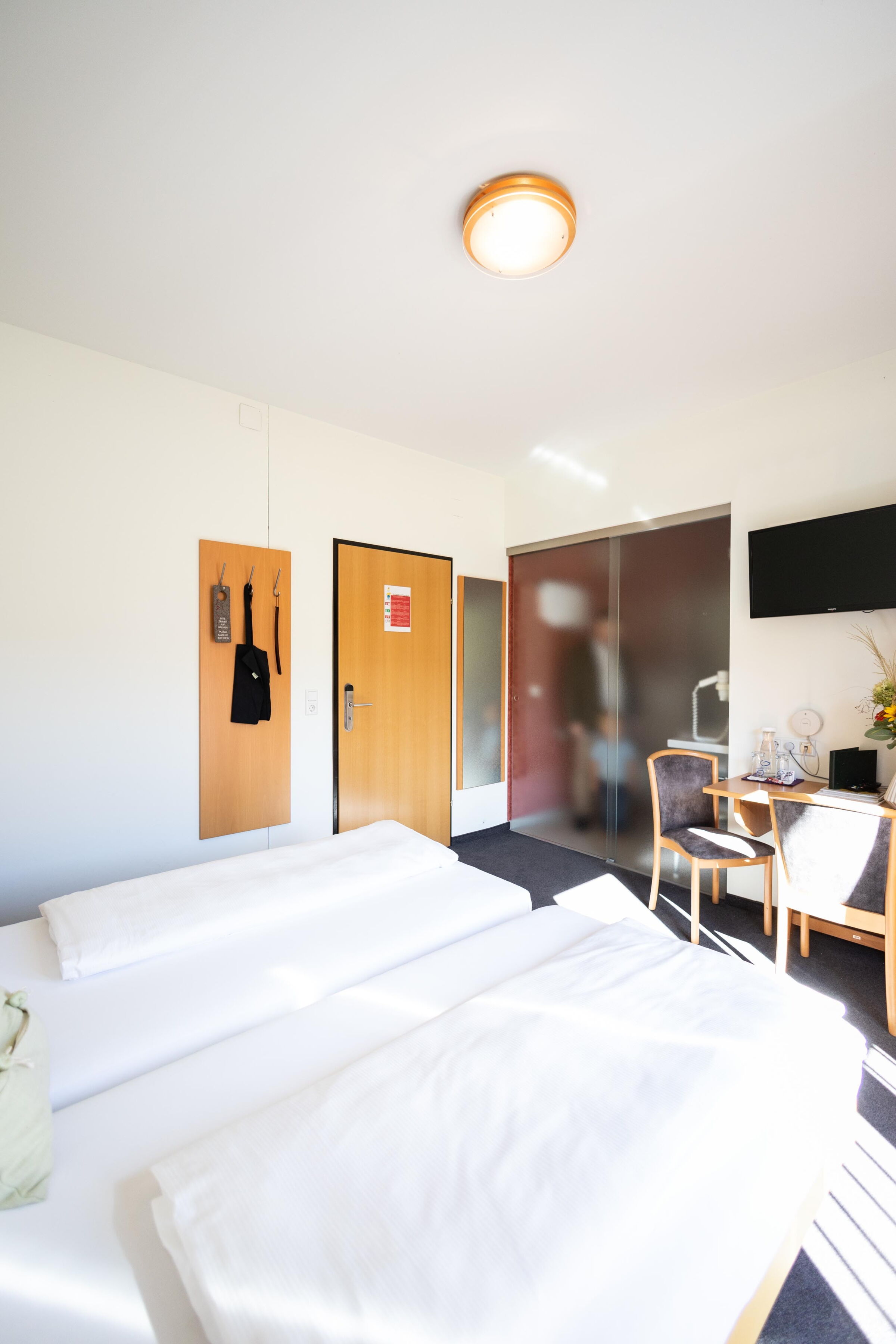 Bright room with double bed, TV, desk and coat hooks on the wall.