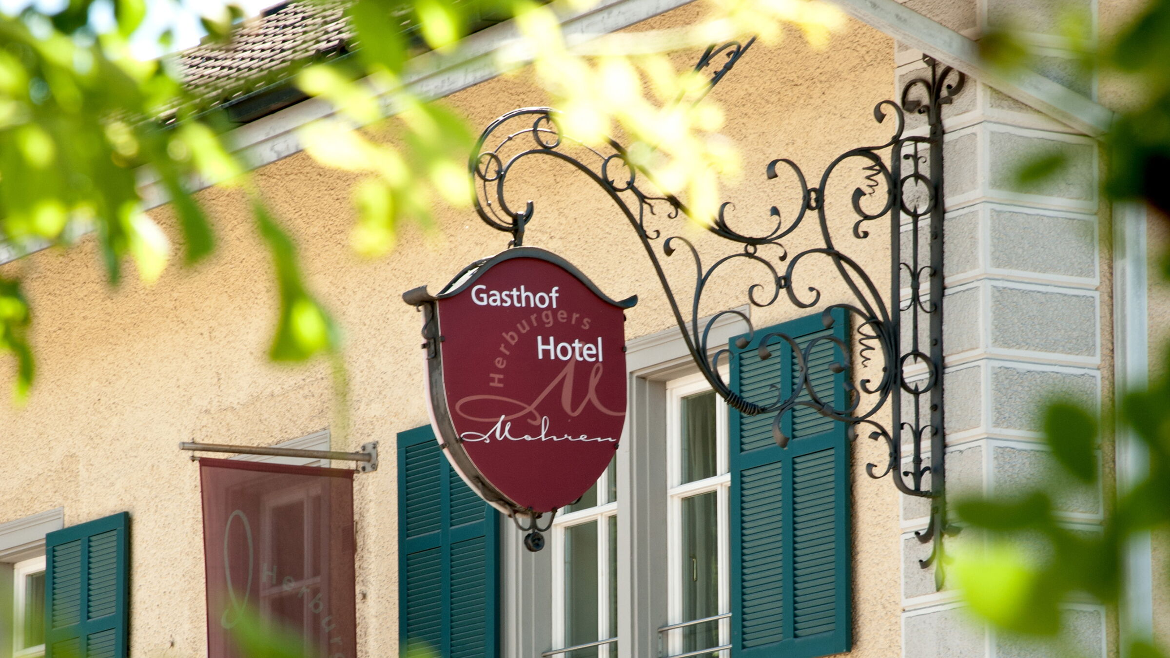 Schild des Gasthof Hotel Mohren mit grünen Fensterläden im Hintergrund.