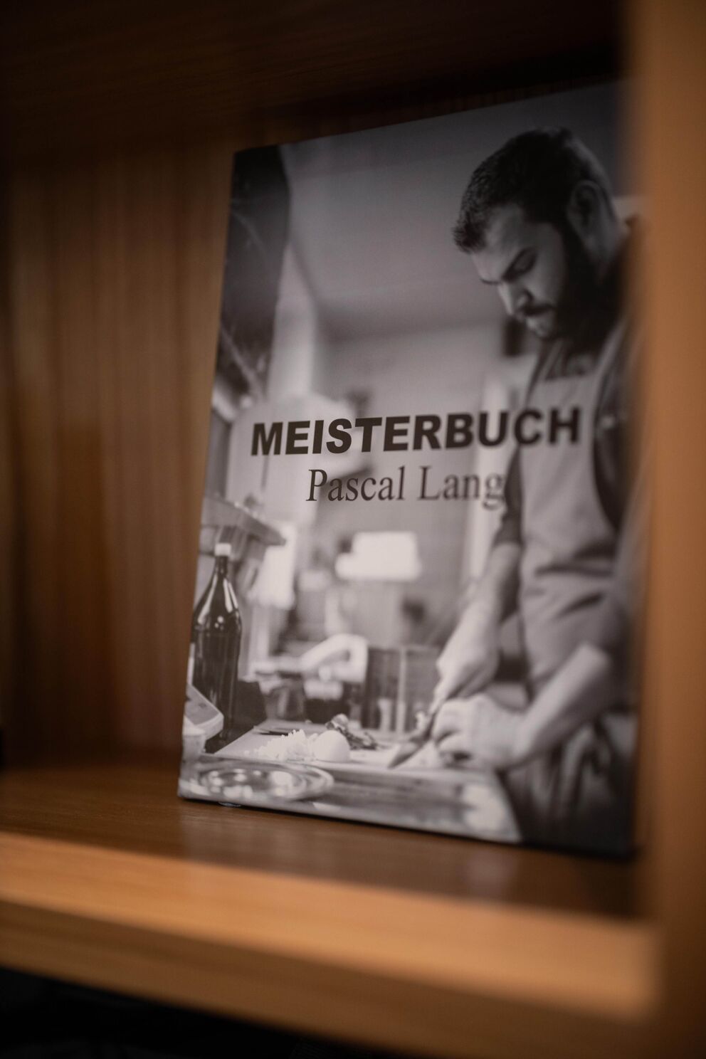 Kochbuch von Pascal Lang mit kulinarischen Anleitungen auf Holzregal.