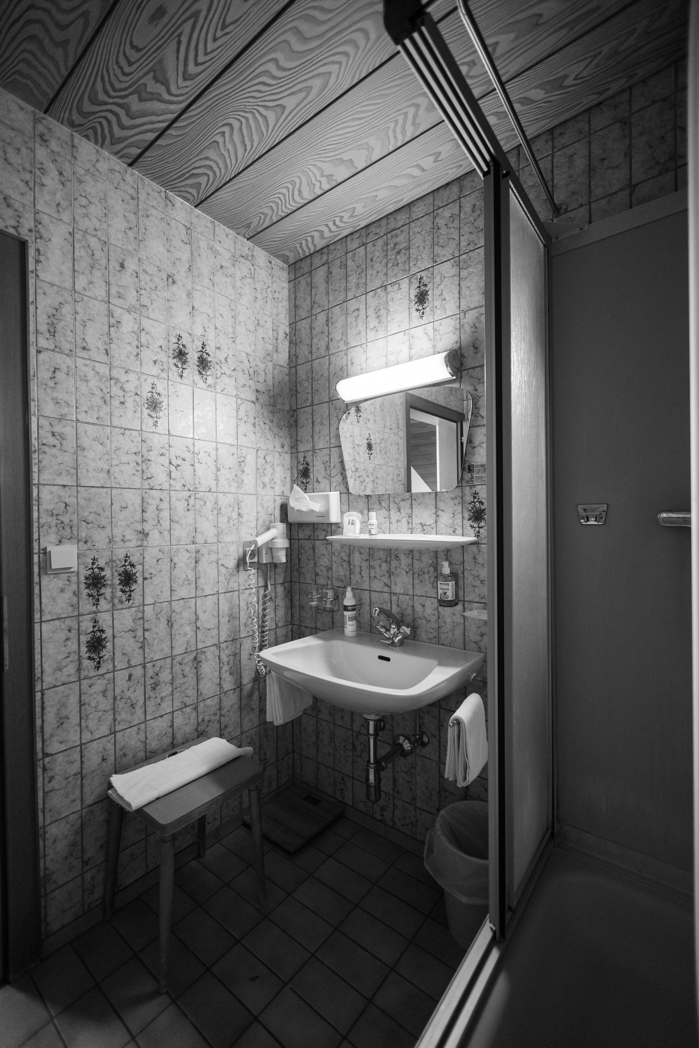Badezimmer mit klassischer Fliesenoptik, Waschbecken, Spiegel und Duschbereich in Vintage-Stil.