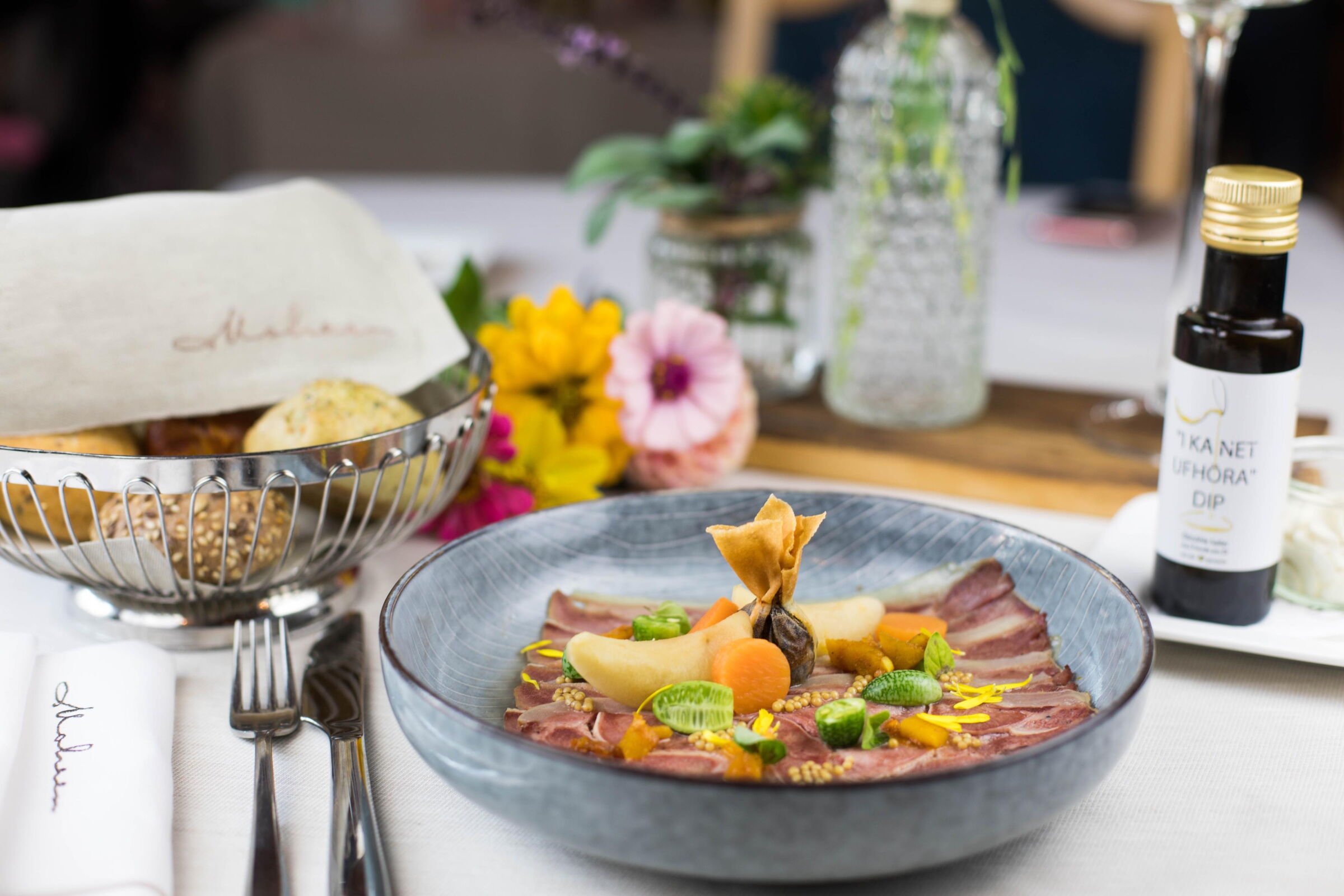 Elegant angerichtetes Gericht mit frischen Zutaten, Blumen und regionalem Dip.