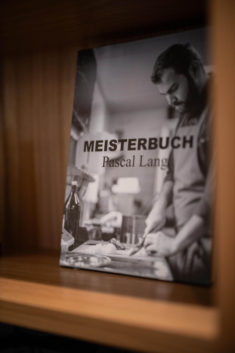Kochbuch von Pascal Lang mit kulinarischen Anleitungen auf Holzregal.
