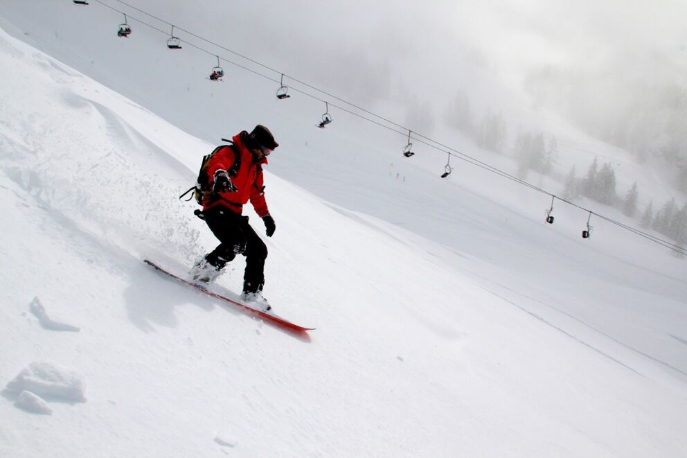 Person snowboarding in a snowy mountain landscape under ski lifts in foggy weather.