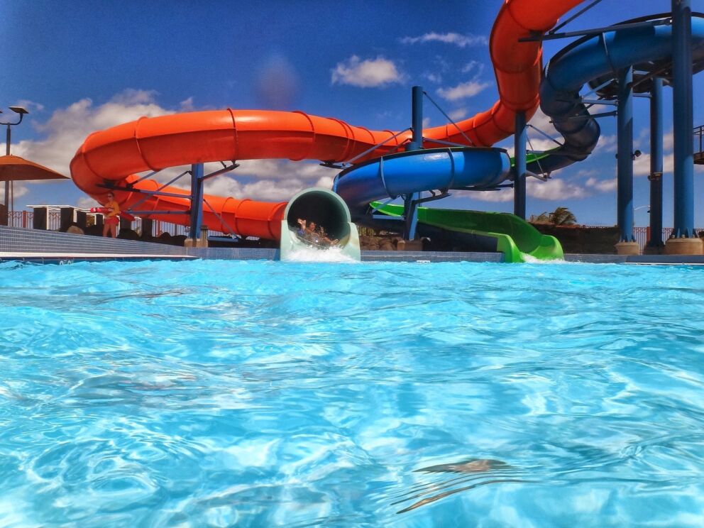 Bunte Wasserrutschen münden in ein großes Schwimmbecken unter blauem Himmel.