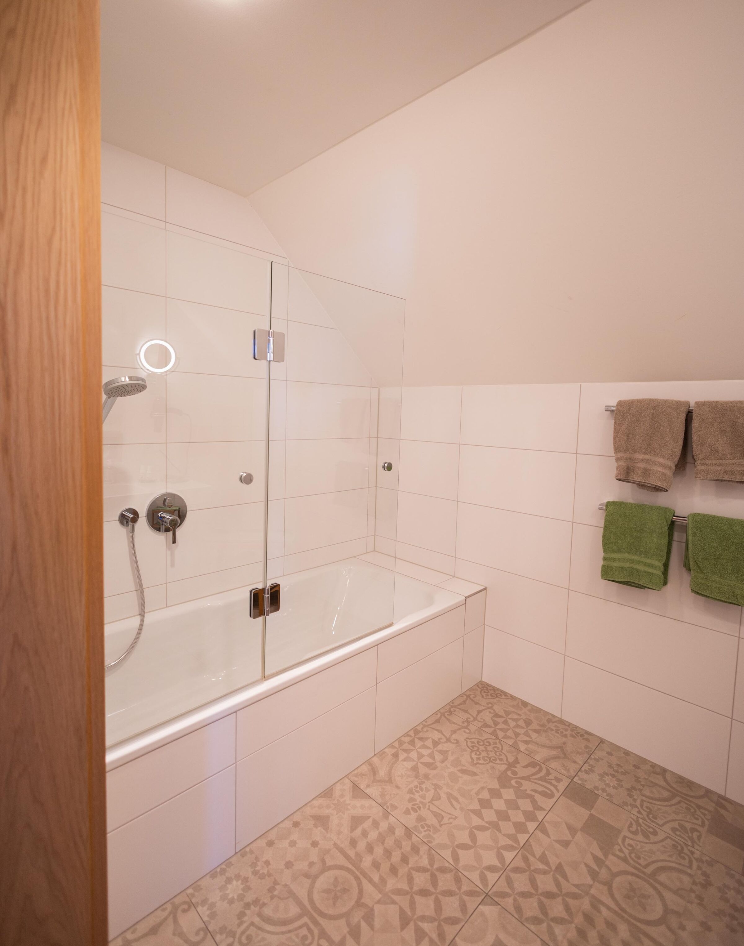 Bright bathroom with bathtub, glass partition and hand-picked towels.