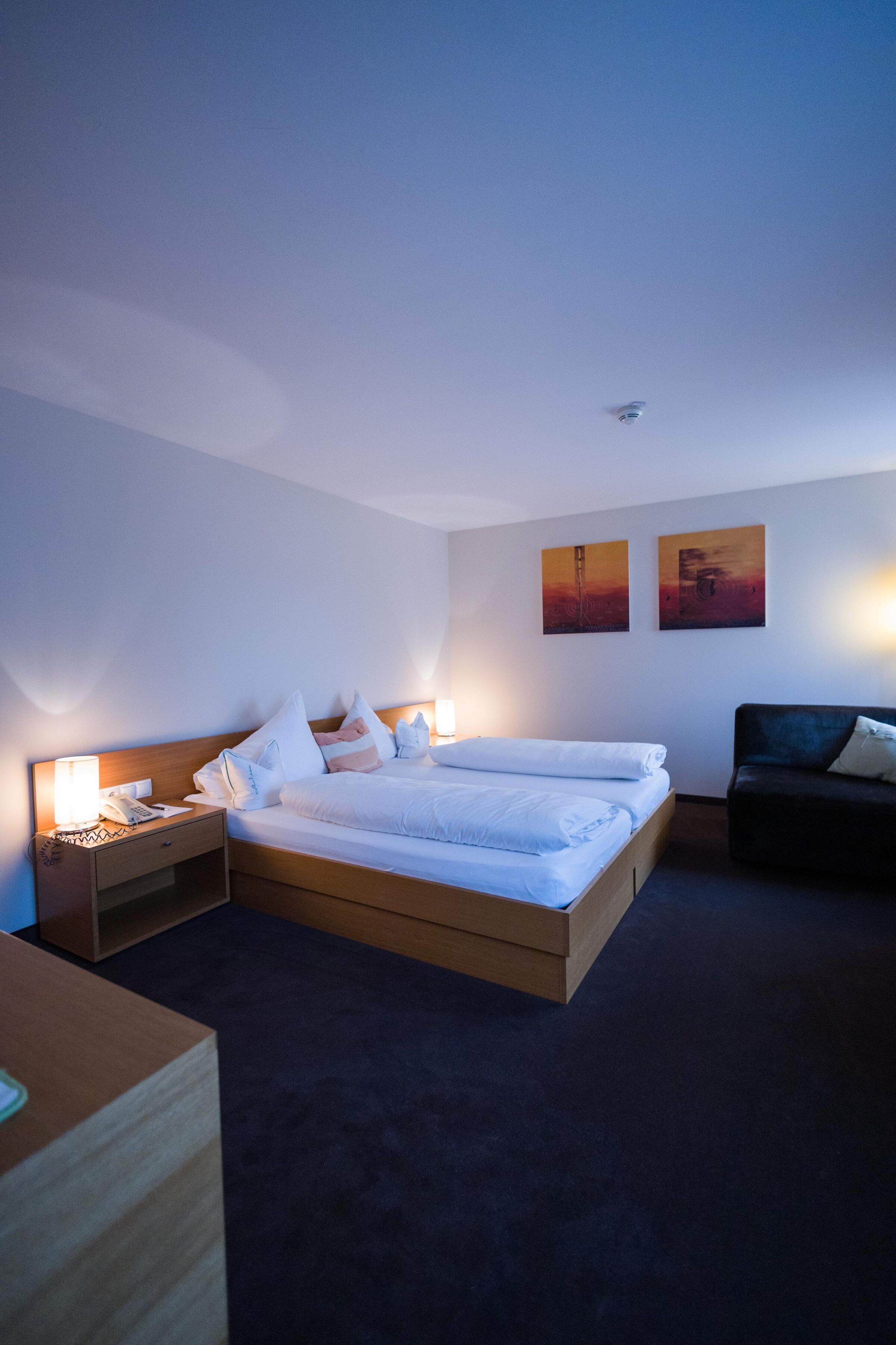 Helles Doppelzimmer mit Holzmöbeln, gemütlichen Kissen und sanfter Beleuchtung.