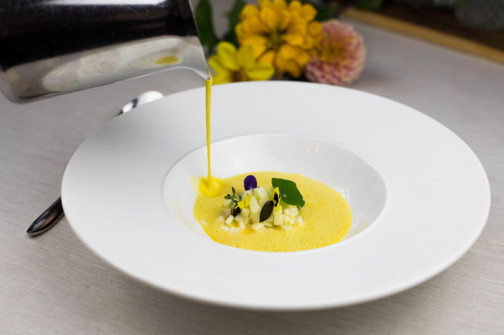 Yellow soup is artfully poured into a plate with a flower and herb garnish.