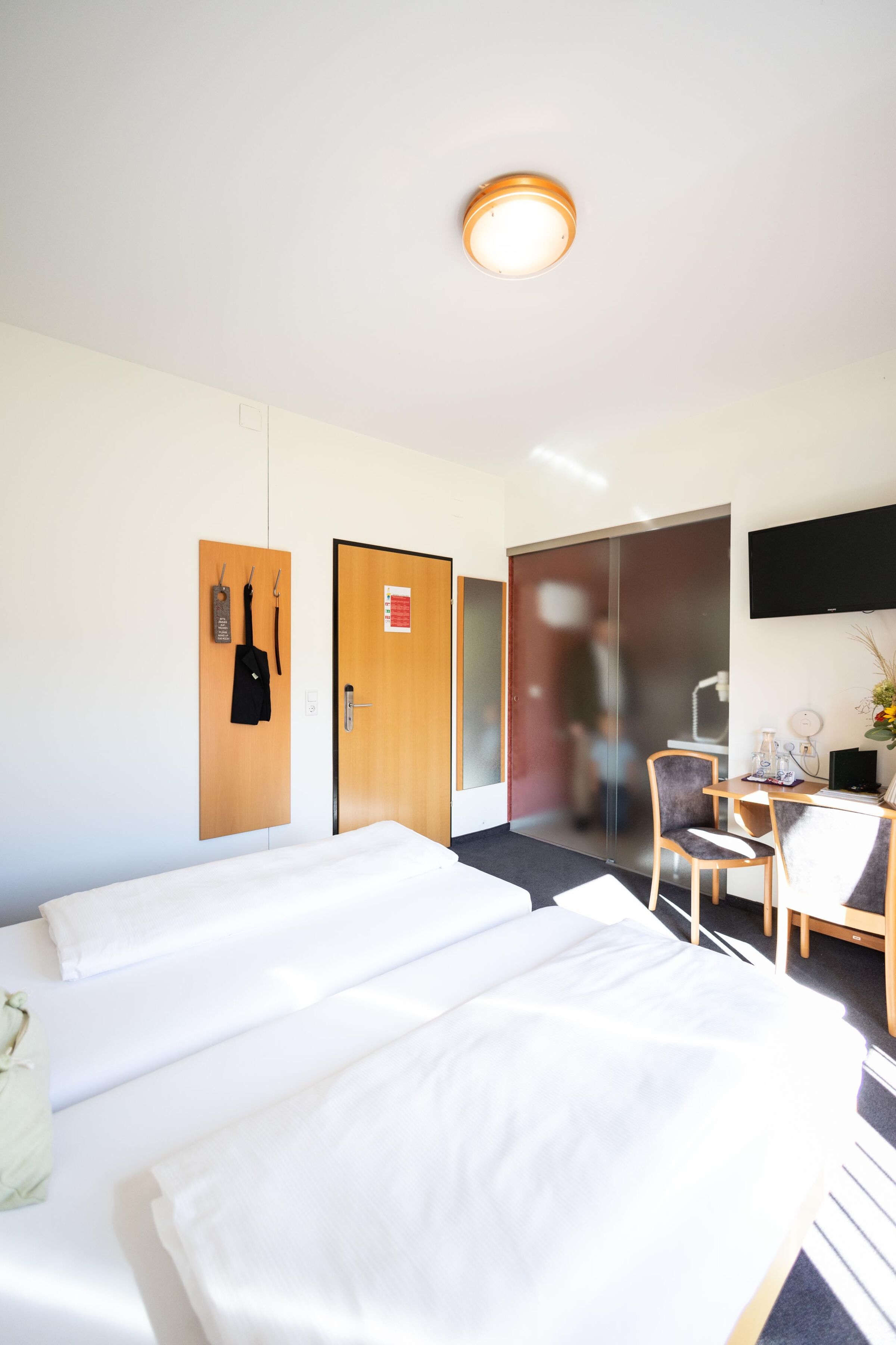 Bright room with double bed, TV, desk and coat hooks on the wall.