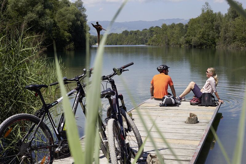 Two people sit on a jetty with bicycles and enjoy the view.