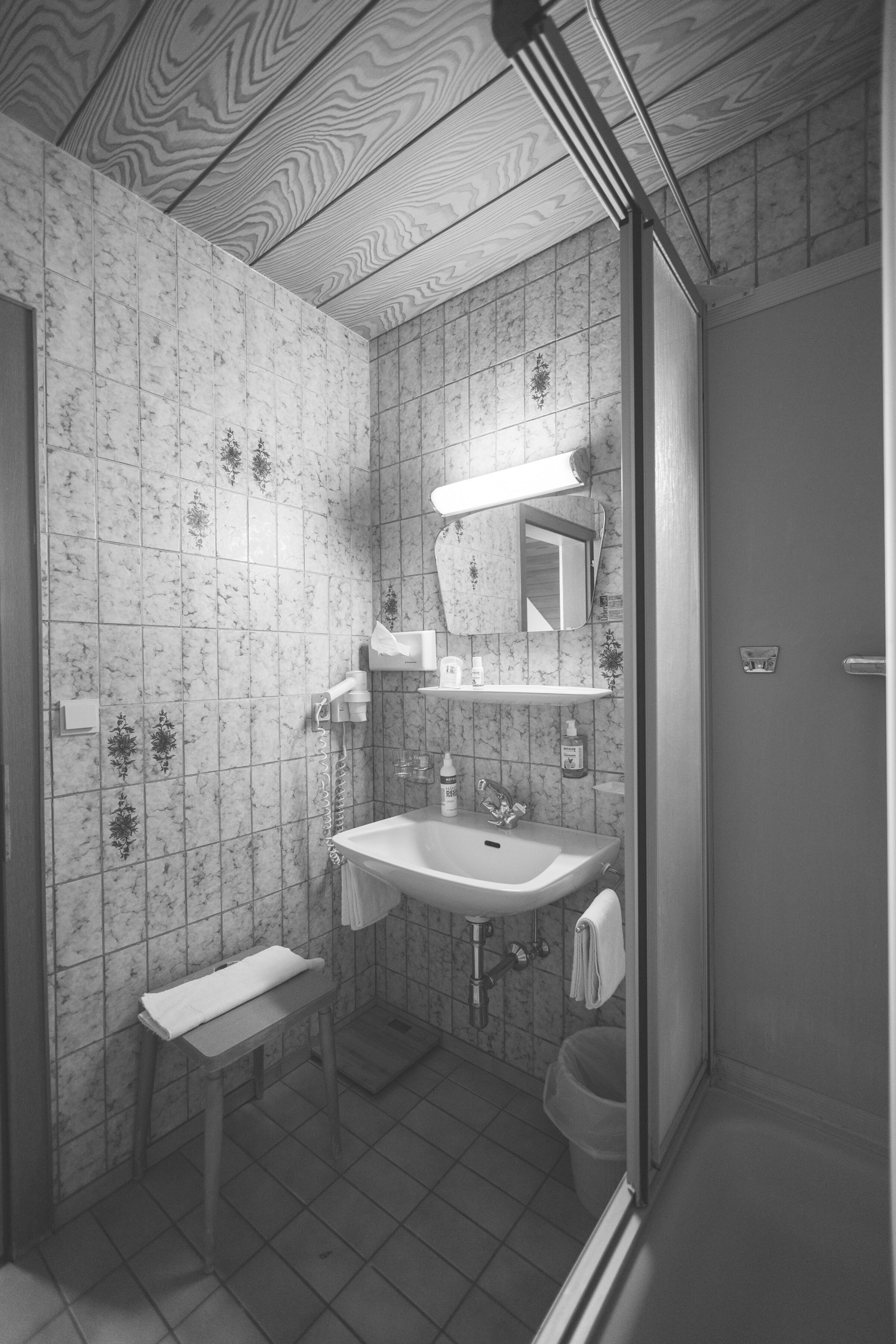 Badezimmer mit klassischer Fliesenoptik, Waschbecken, Spiegel und Duschbereich in Vintage-Stil.