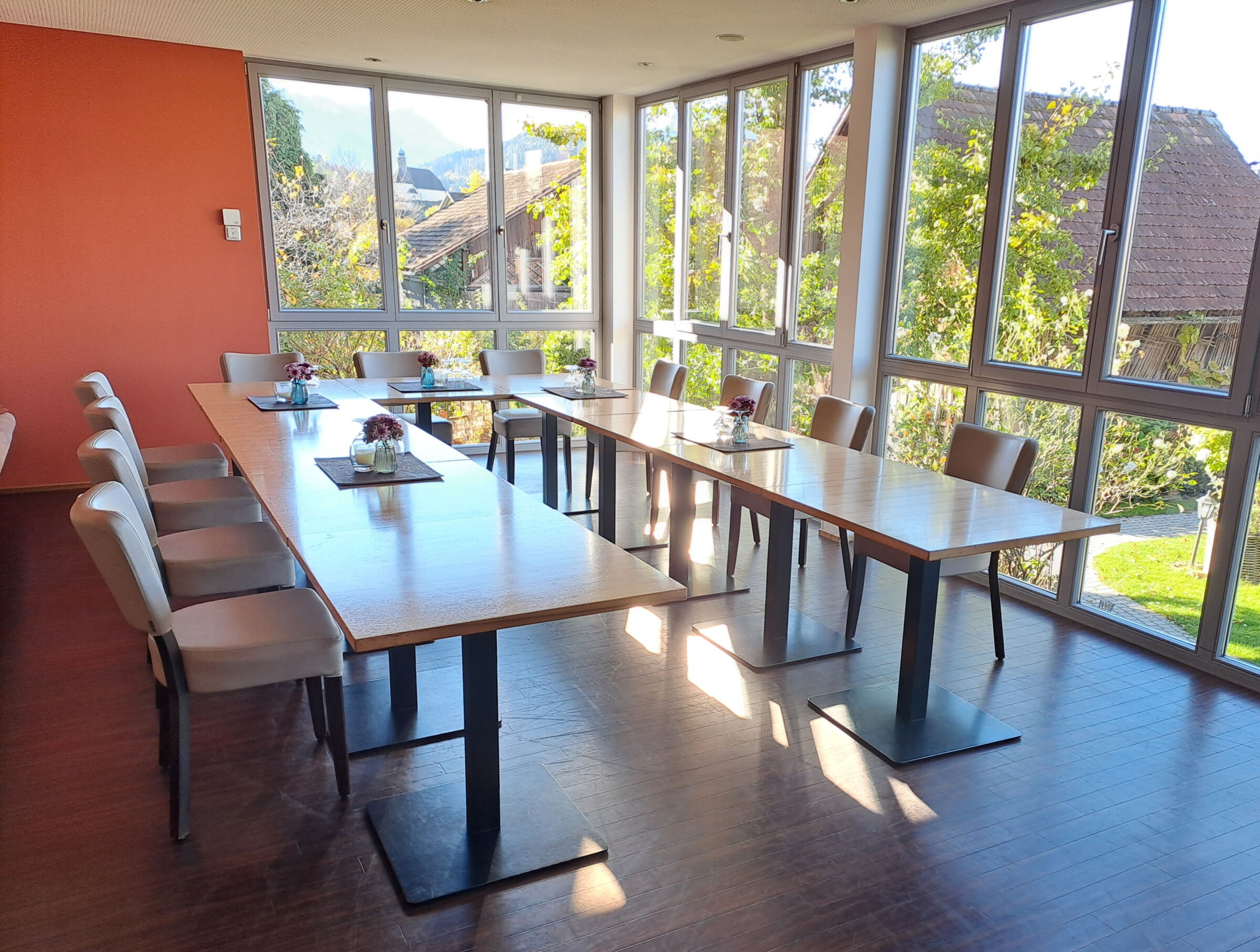 Großer Konferenzraum mit Holztischen und Panoramafenstern, Blick auf Garten.