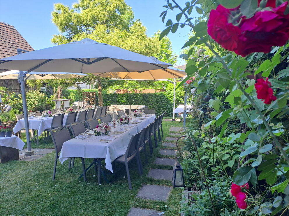 Elegant garden tables with white tablecloths and flower arrangements under parasols.