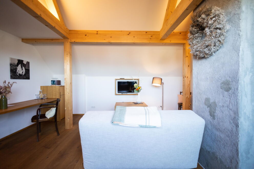 Helles Zimmer mit Holzbalken, gemütlicher Couch, TV und stilvoller Dekoration.