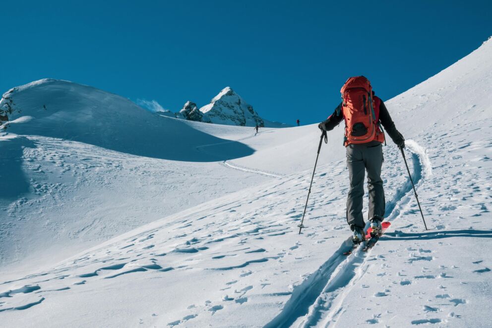 Ski tourers on a snow-covered slope under a clear blue sky in an alpine setting.