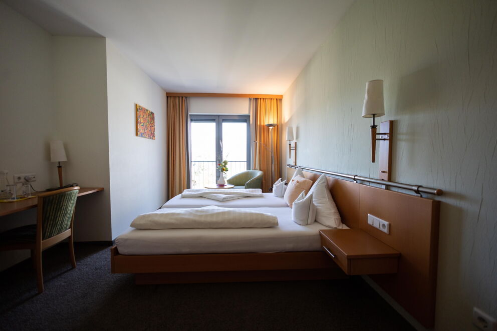 Bright room with double bed, desk, window and decorative wall art.