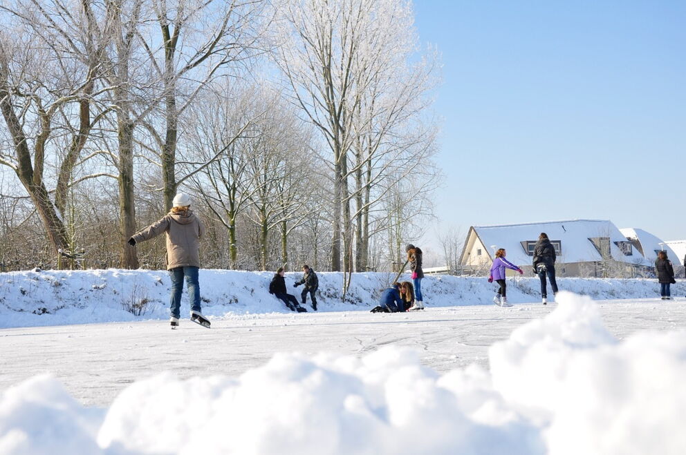 Menschen genießen Eislaufen auf zugefrorenem See in verschneiter Landschaft.