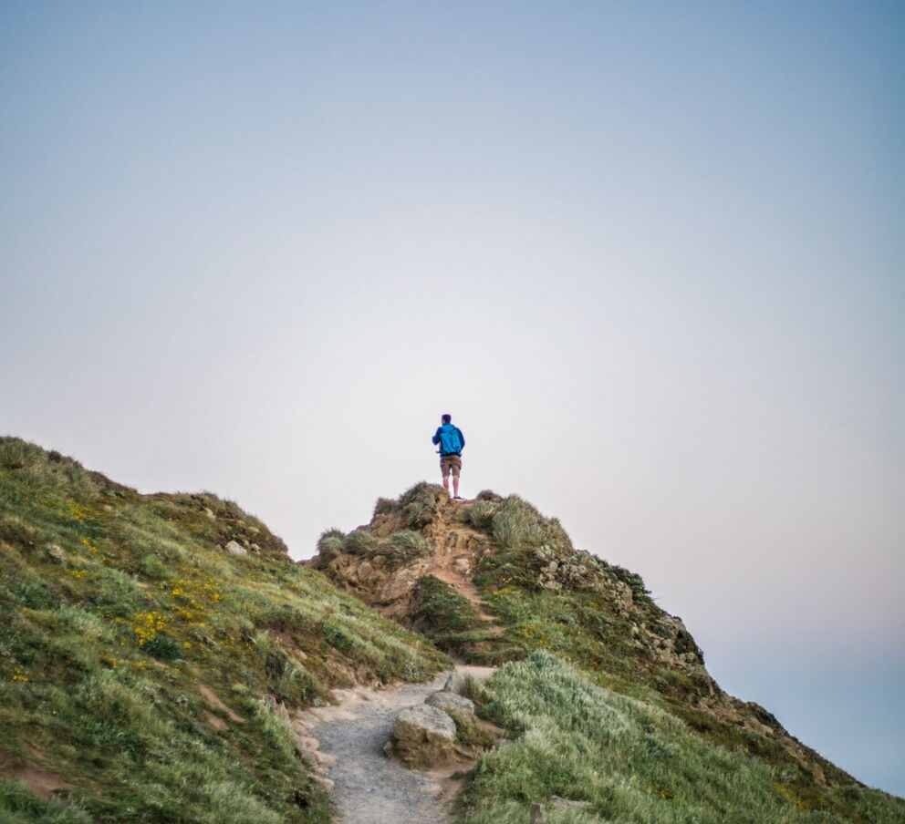 Person walking on grassy hill under clear sky in daylight.