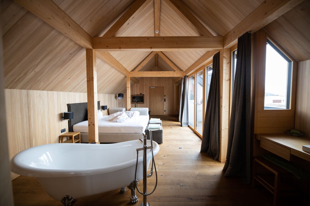Helles Zimmer mit freistehender Badewanne, Holzverkleidung und großen Fenstern.