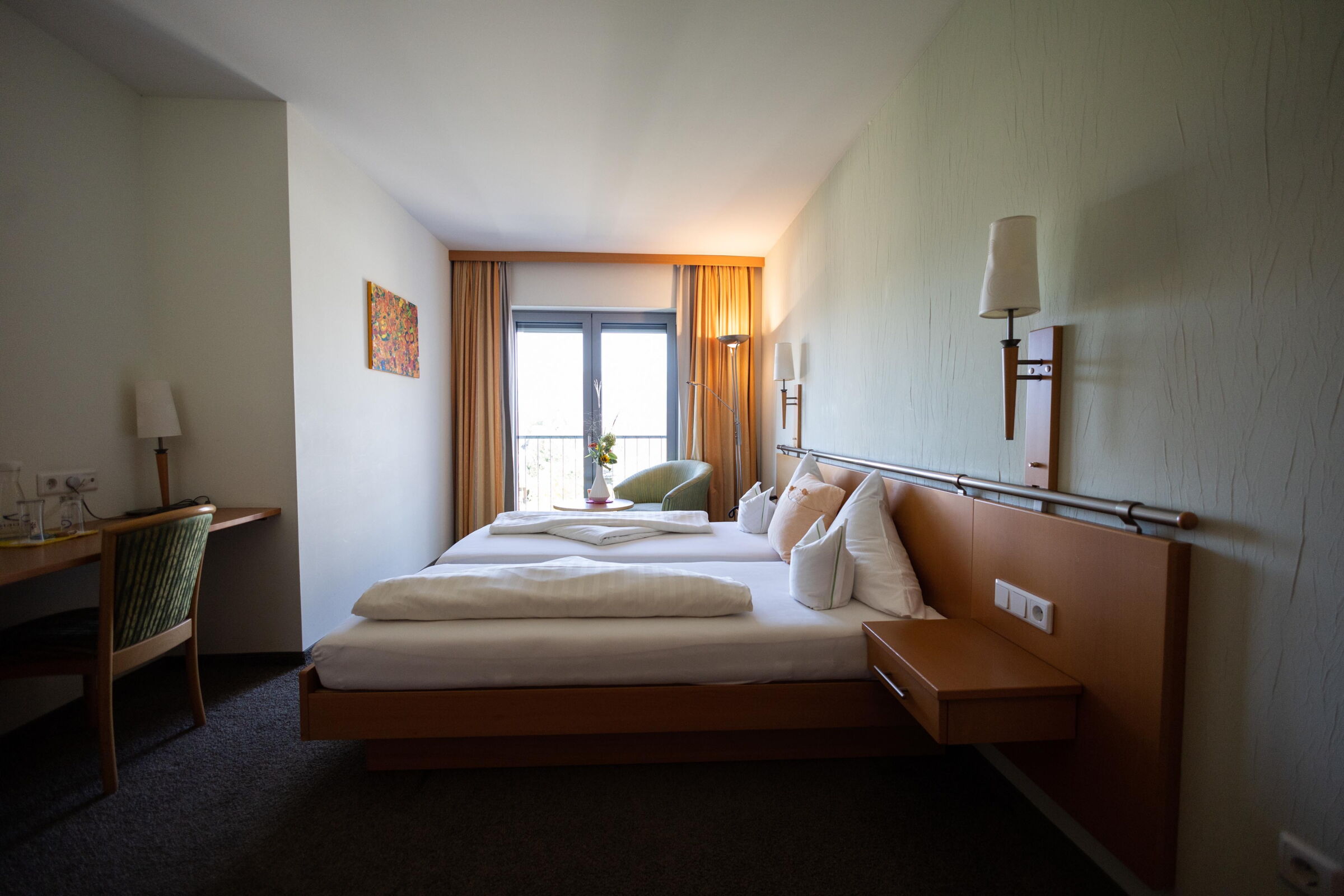 Bright room with double bed, desk, window and decorative wall art.
