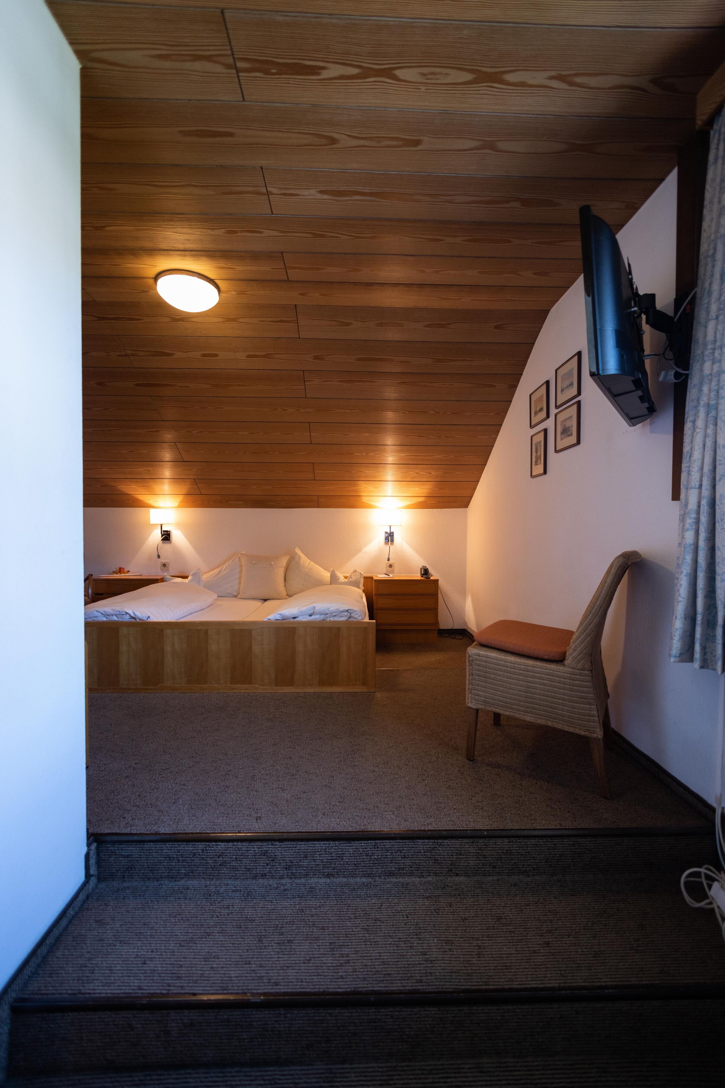 Gemütliches Zimmer unterm Dach mit Holzelementen, Bett und warmem Licht.