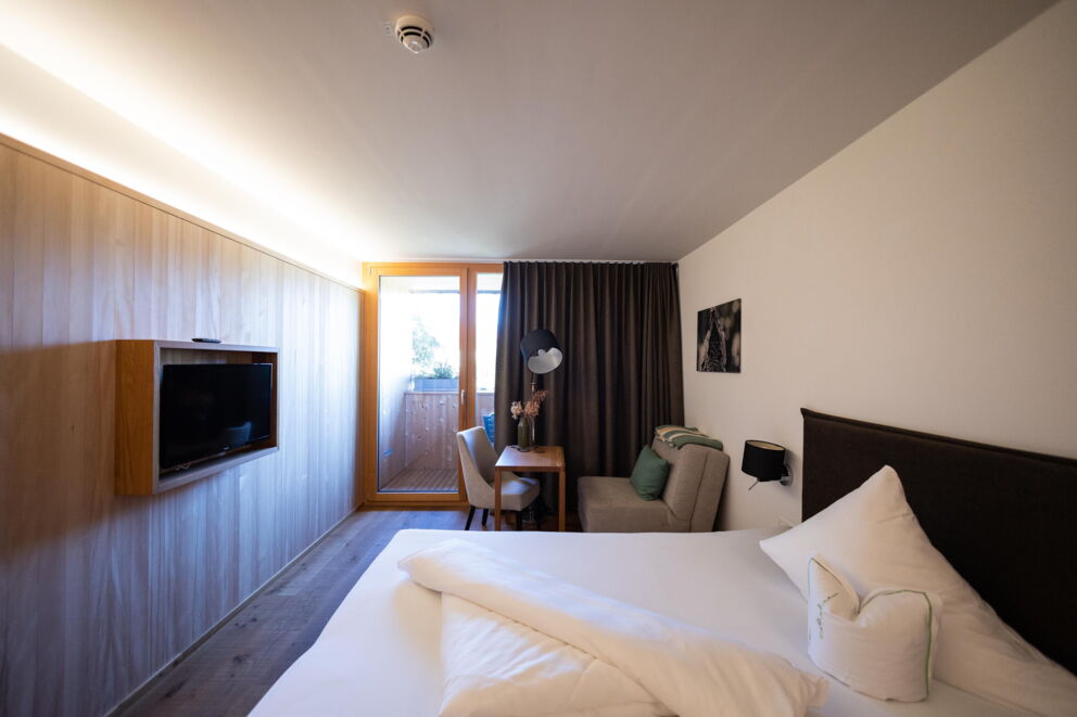 Modern furnished hotel room with balcony and cozy seating area.