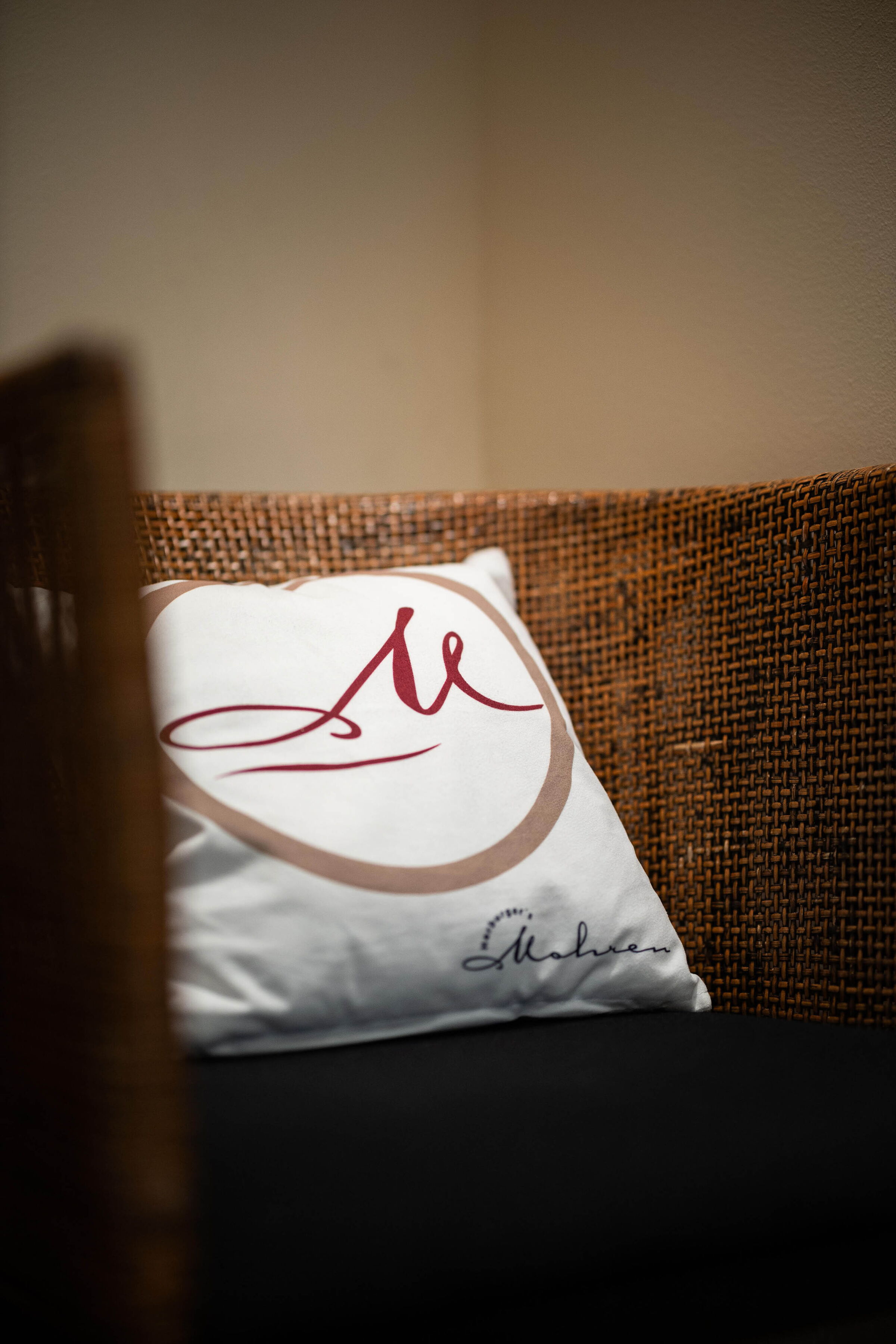 White cushion with Mohren logo on a woven chair in a warm setting.