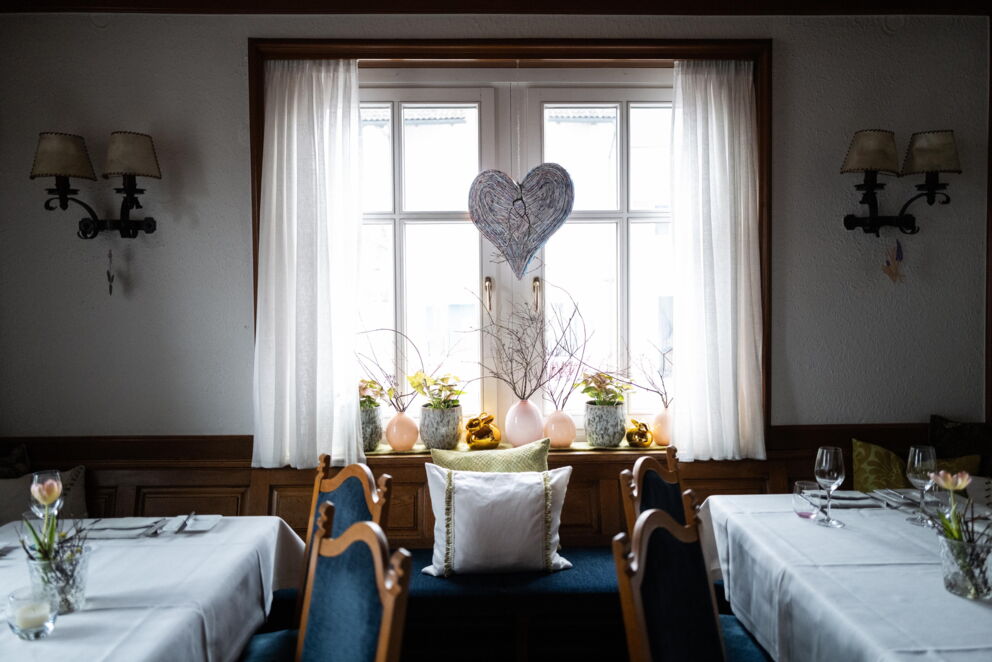Elegant window with heart decoration, surrounded by plants and laid tables.