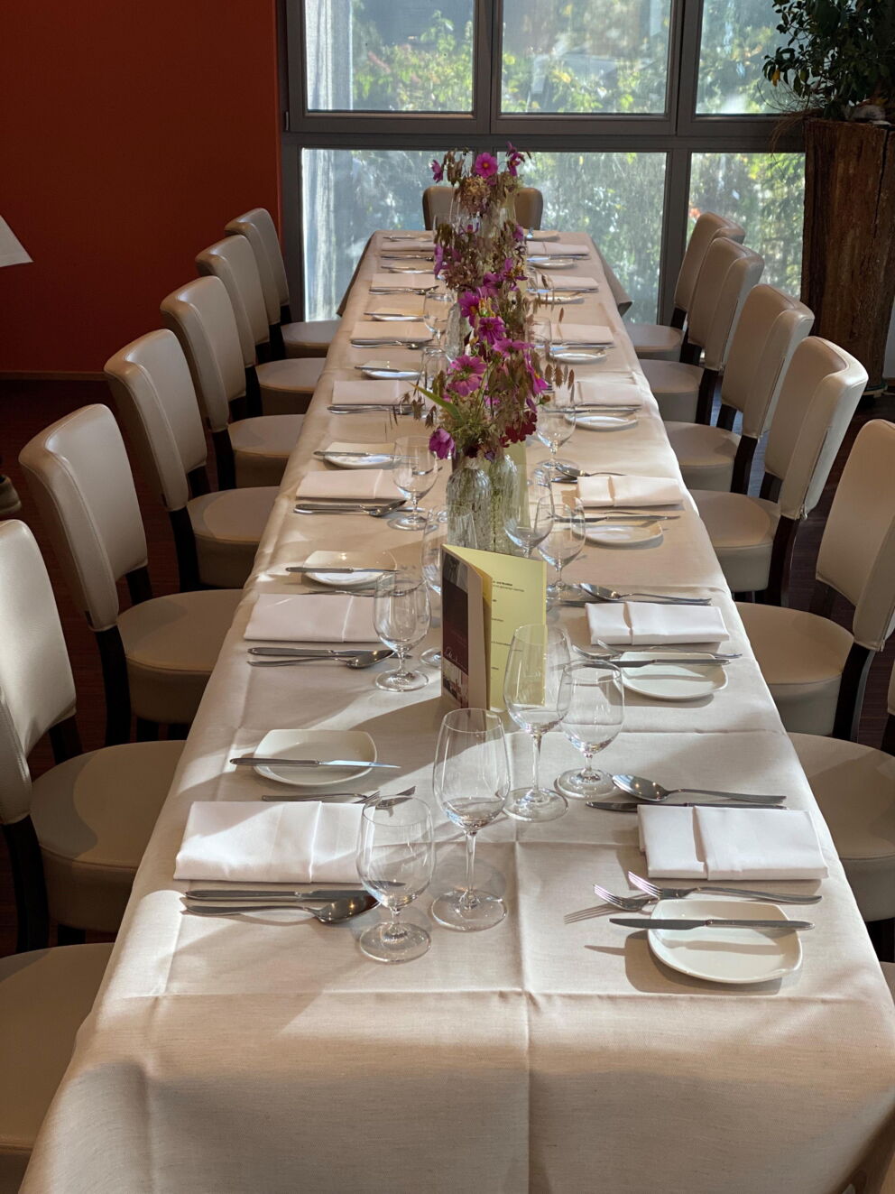 A festively laid table with flower arrangements and laid plates in a bright room.