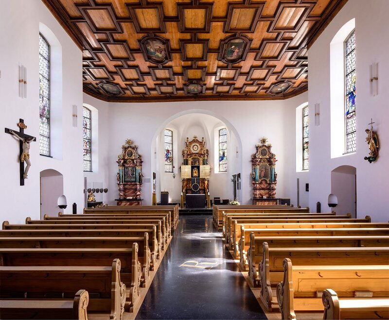 Interior of a church with wooden benches, decorated altars and stained glass windows.