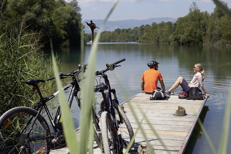 Zwei Personen sitzen auf einem Steg mit Fahrrädern und genießen die Aussicht.