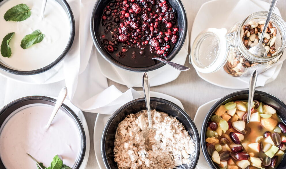 Five bowls of yogurt, berries, muesli and fresh fruit on a table.