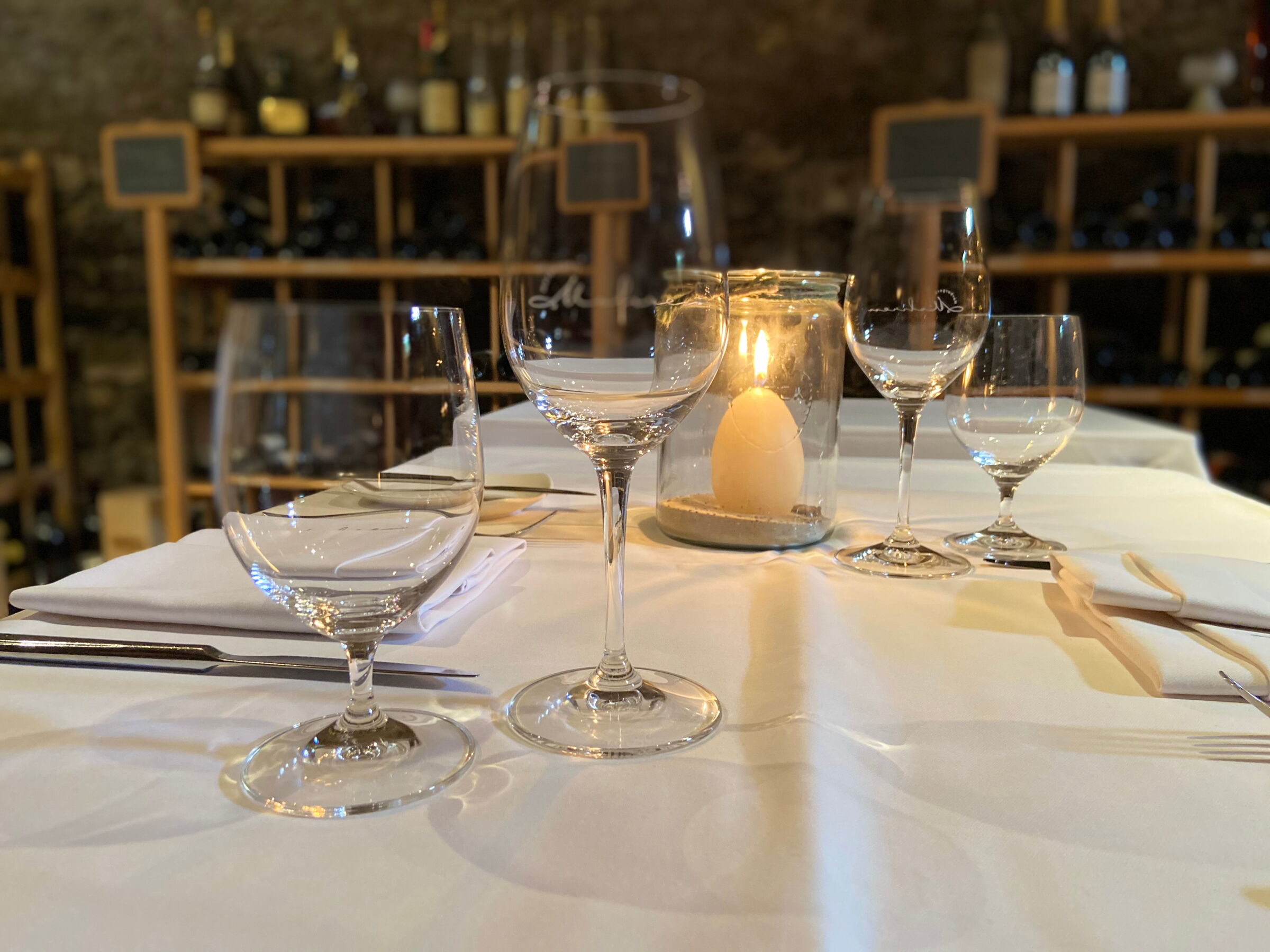 Elegante Weingläser und Kerzenlicht auf festlich gedecktem Tisch im Weinkeller.