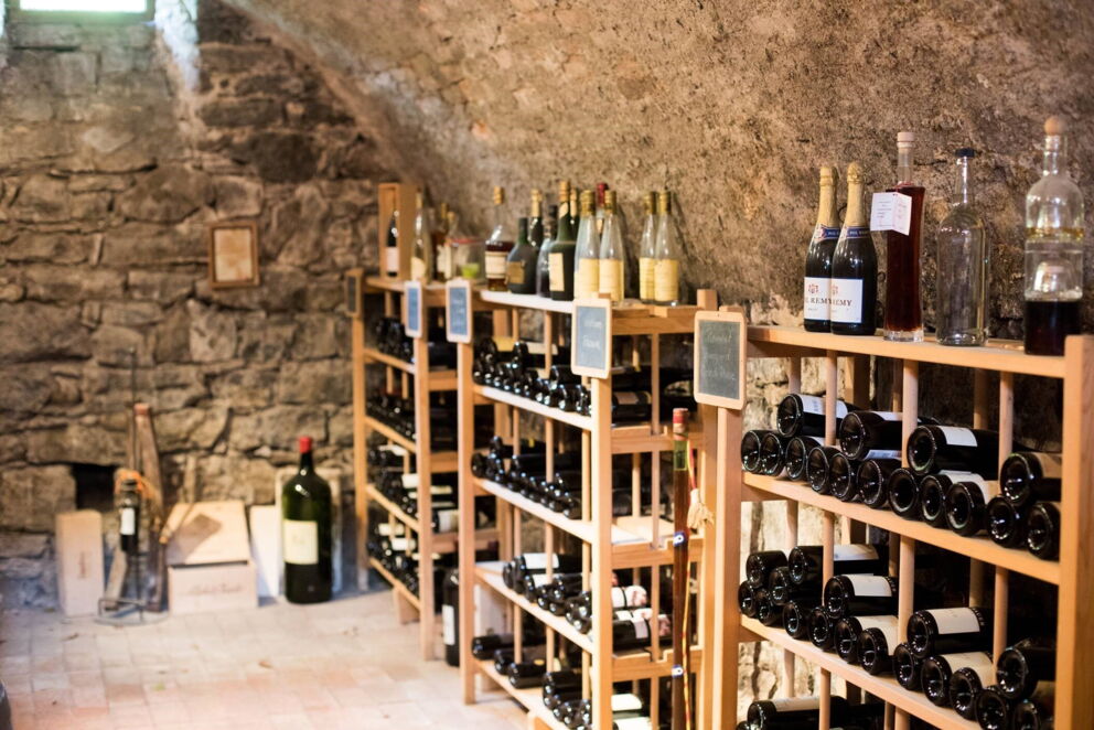 Rustikaler Weinkeller mit gefüllten Holzregalen und sichtbaren Steinwänden.