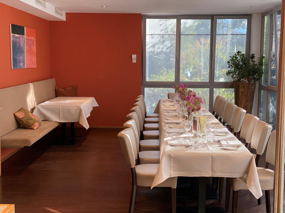 Long table in stylishly furnished corner with windows and red wall.