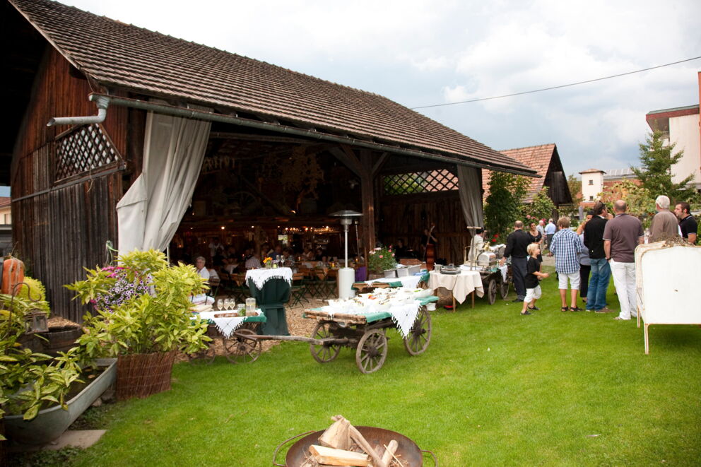 Menschen genießen ein Event im grünen Erlebnisgarten mit gedeckten Tischen und Blumen.