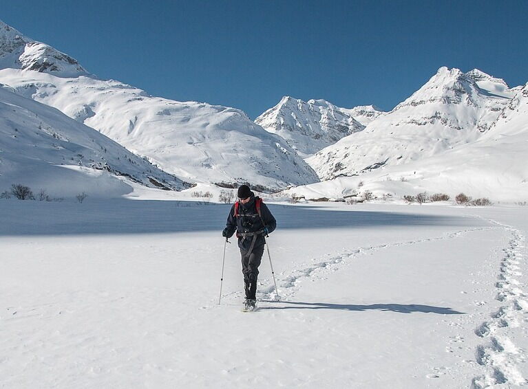 Person wandert durch verschneite Berglandschaft unter klarem blauen Himmel.