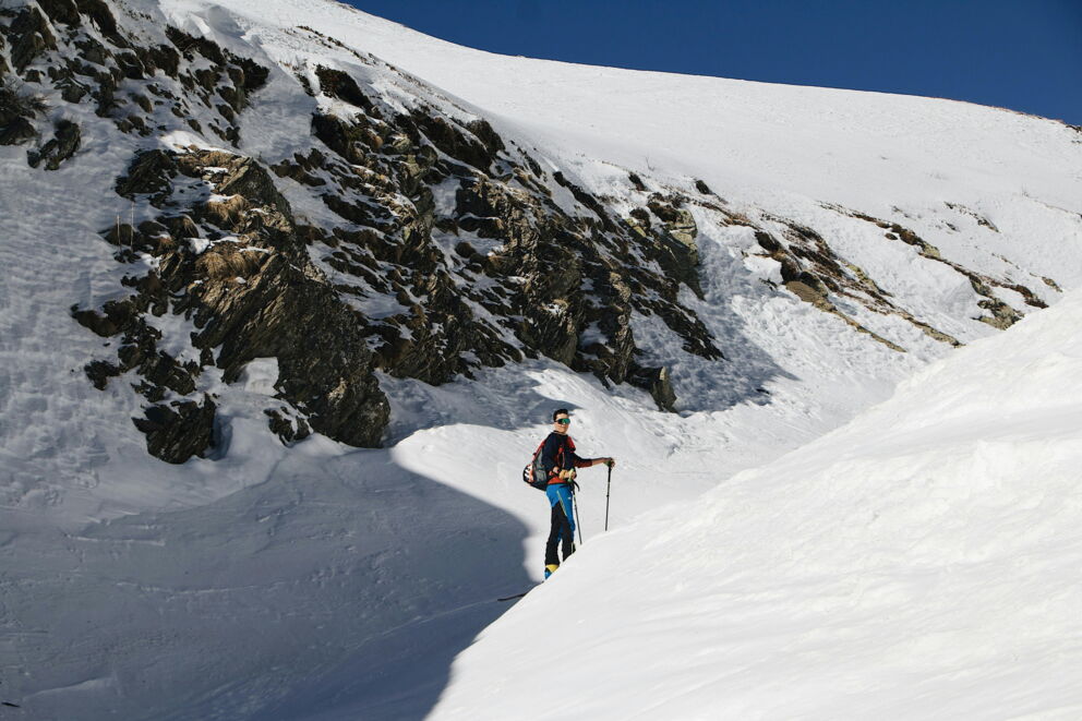 Person ski touring in a snow-covered mountain landscape with a blue sky