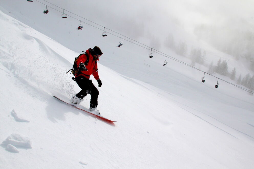 Person snowboarding in a snowy mountain landscape under ski lifts in foggy weather.