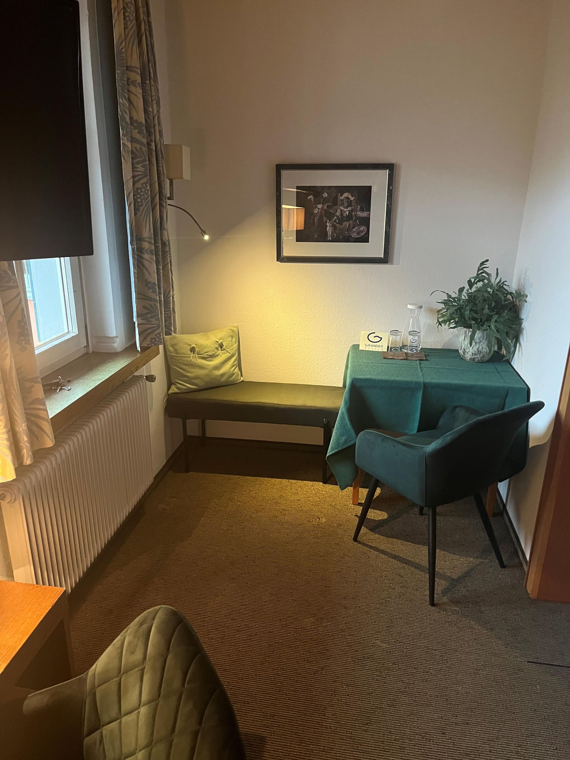 Kleine Sitzecke mit Tisch, Stuhl, Bank und dekorativen Elementen im Hotelzimmer.