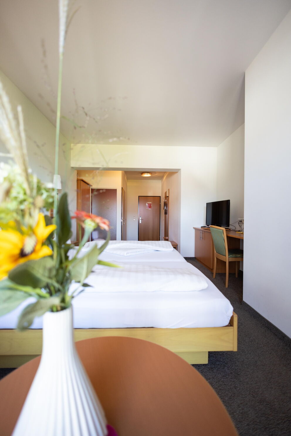 Helles Hotelzimmer mit Blumen in einer Vase und einem Fernseher.