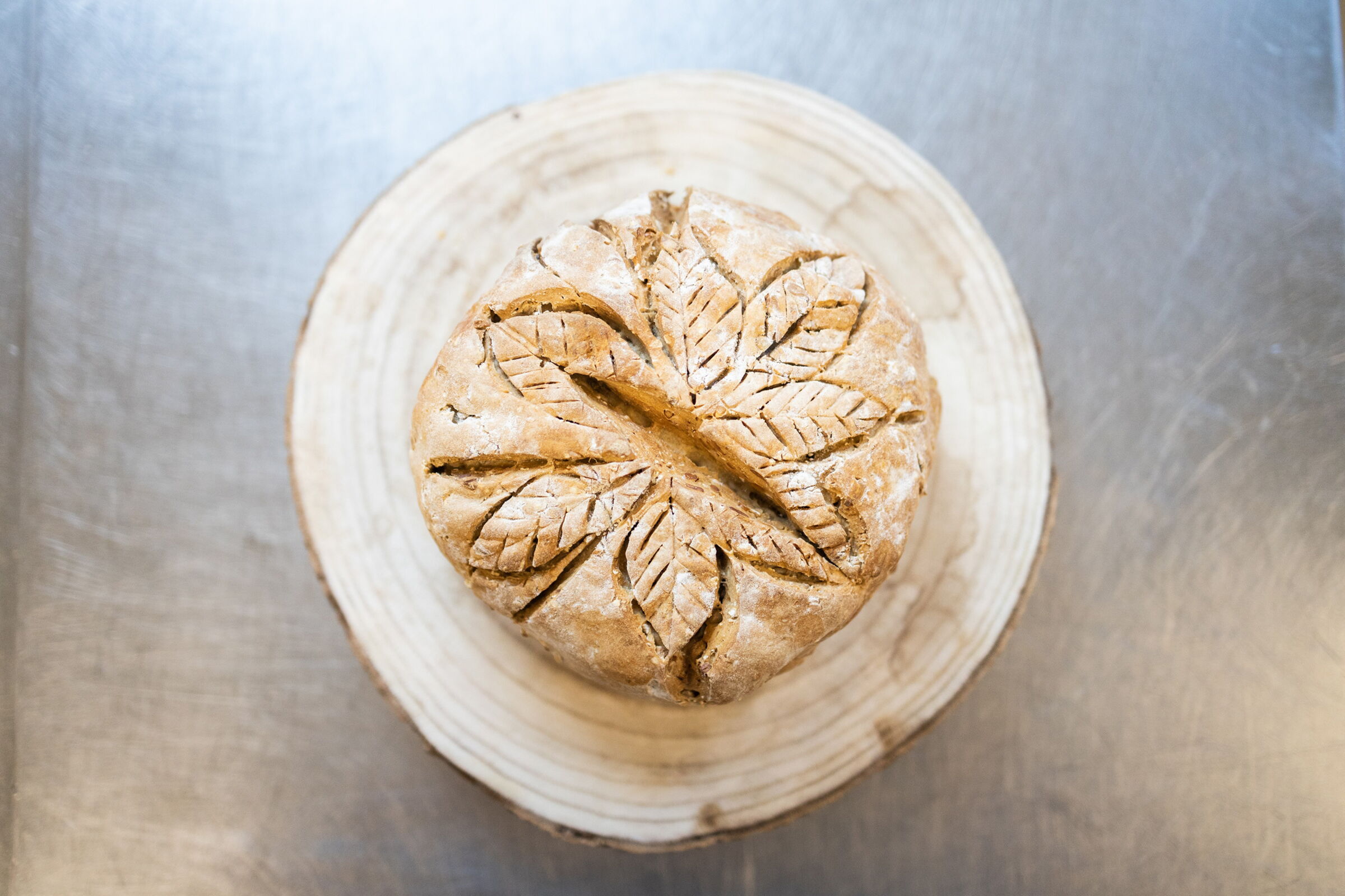 Round loaf with leaf pattern on wooden base, top view.
