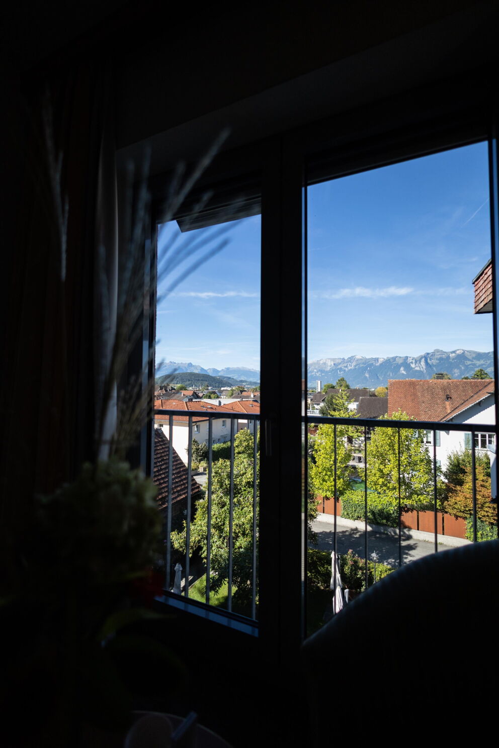 Blick aus dem Fenster auf ein malerisches Dorf mit Alpen im Hintergrund.