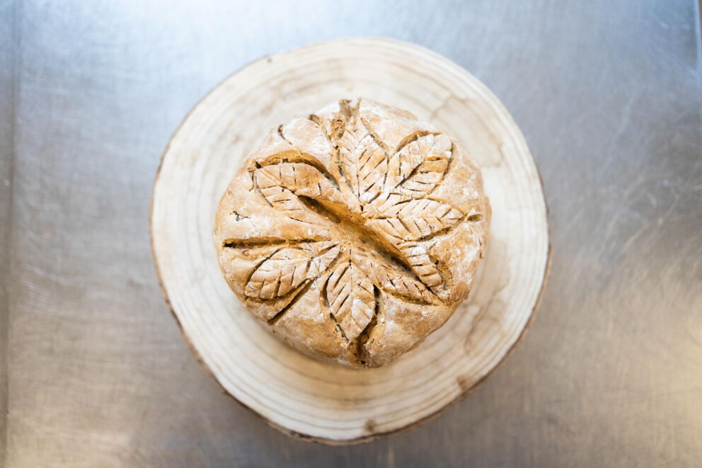 Round loaf with artistically engraved leaves presented on a wooden plate.