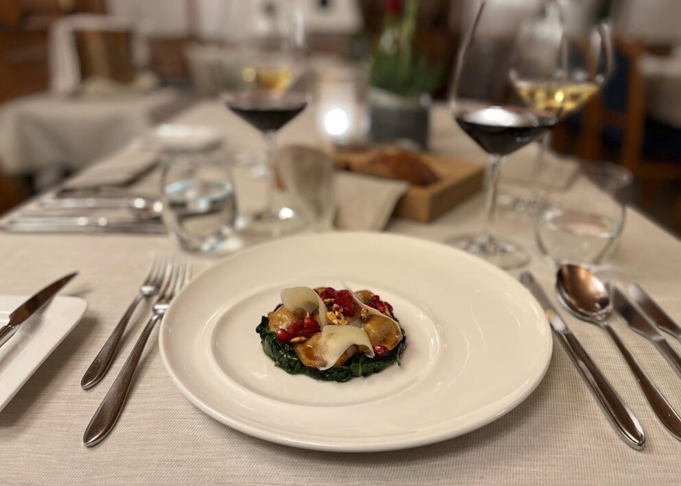 Elegant dish on a white plate, table stylishly set with wine glasses.