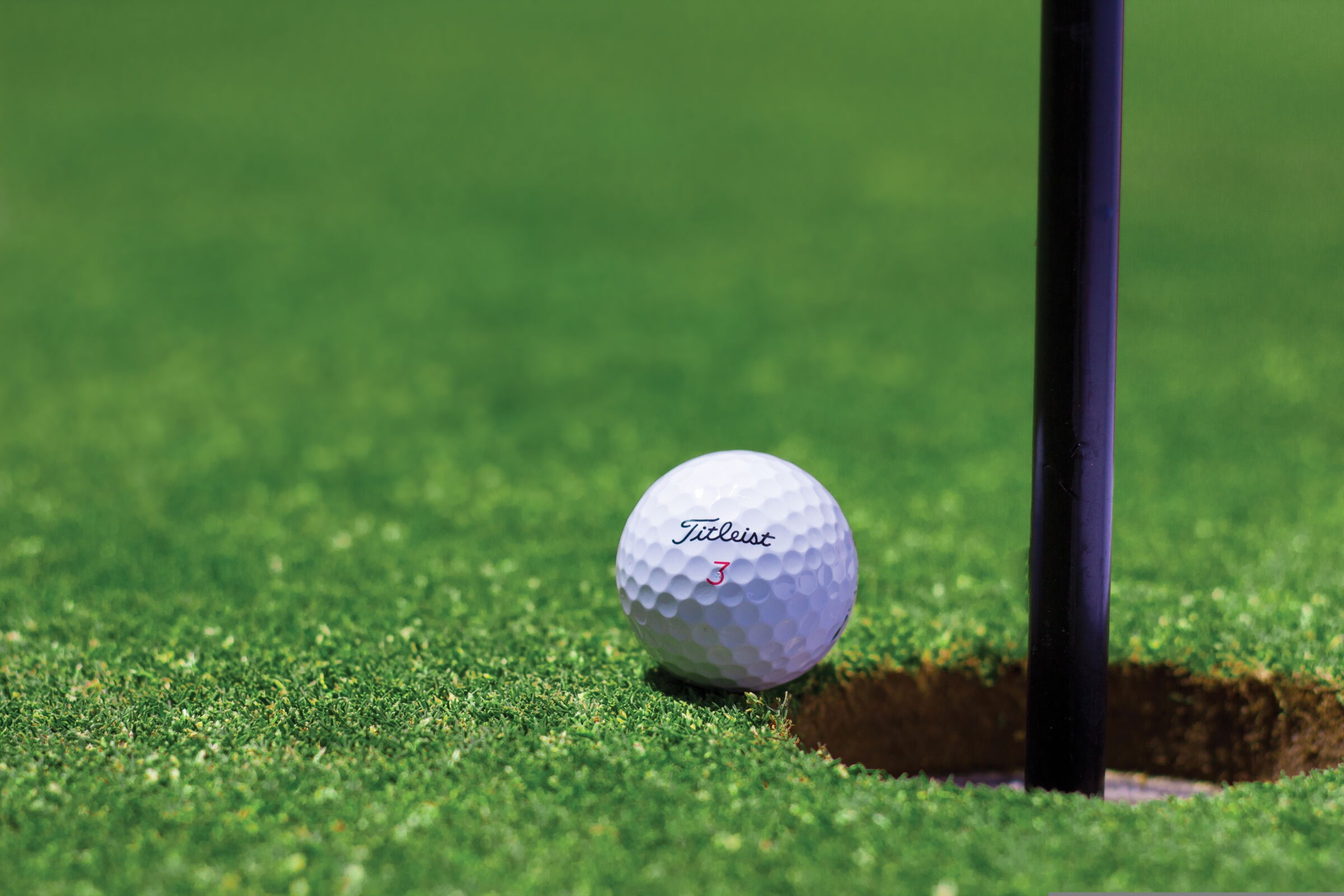 Golf ball lies directly at the hole on green grass.