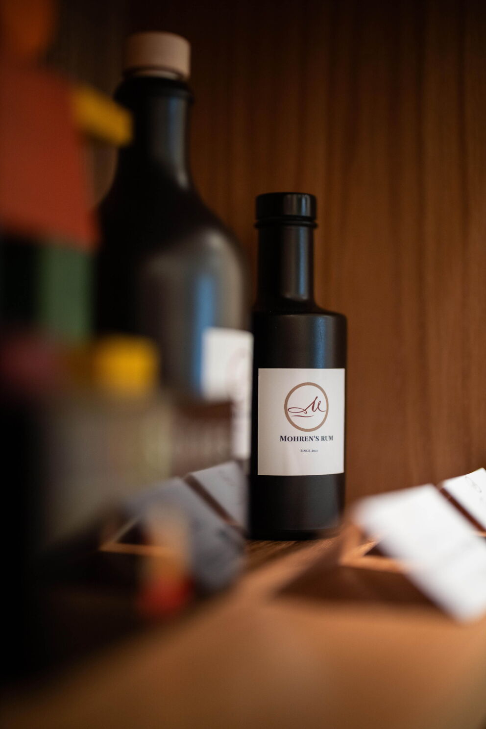 Black rum bottle with elegant label in focus, surrounded by wooden furnishings.
