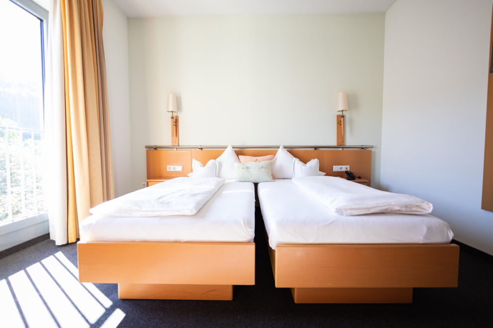 Helles Schlafzimmer mit zwei Betten, großen Fenstern und warmen Holzmöbeln.