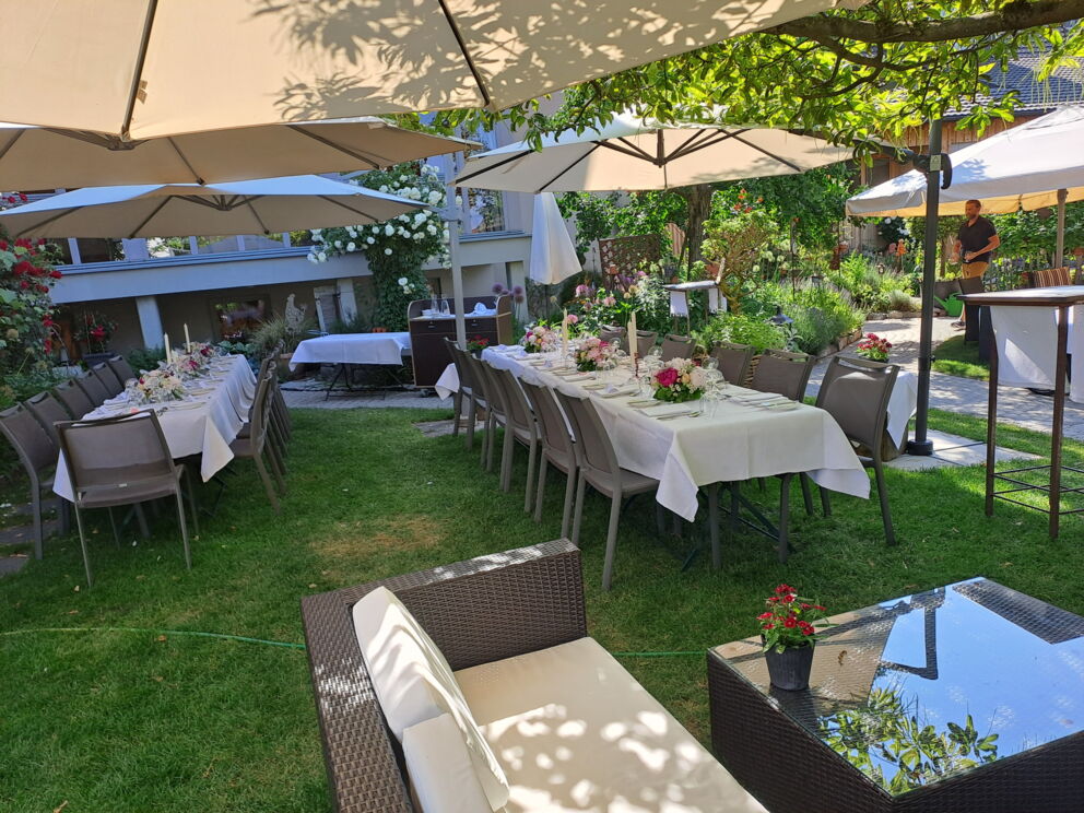 Festlich gedeckte Tische im grünen Erlebnisgarten mit Sonnenschirmen und Blumenarrangements.