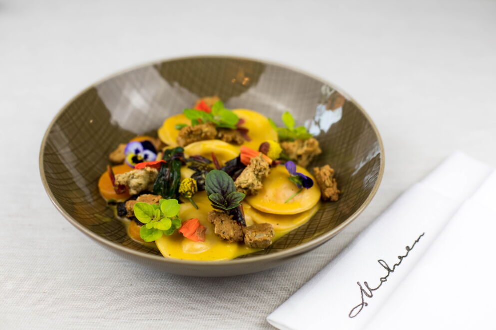 Kunstvoll angerichtete Ravioli mit frischen Kräutern und essbaren Blüten auf elegantem Teller.